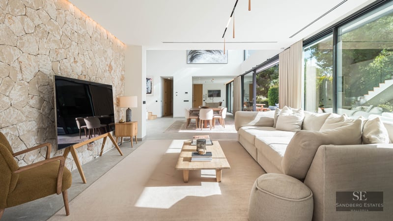 Salon spacieux avec un grand canapé crème, une table basse en bois et un mur d'accent en pierre naturelle claire.