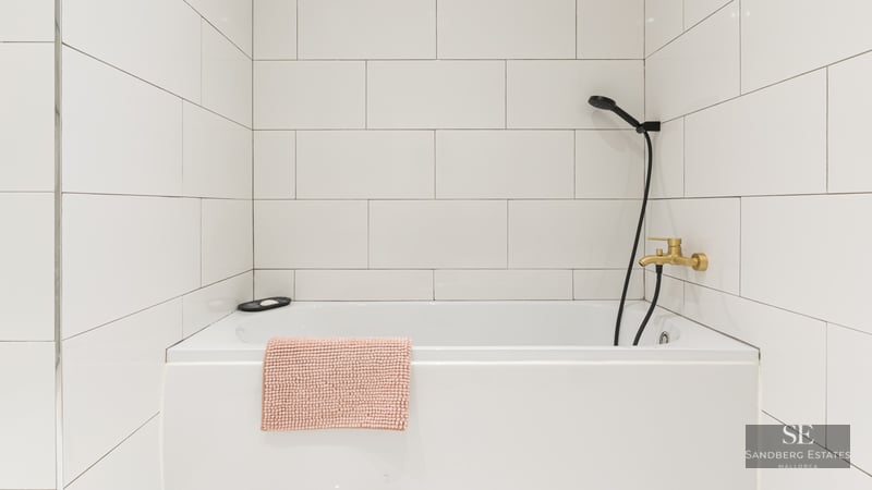 Baignoire blanche, carrelage mural, robinetterie dorée et pommeau de douche noir.