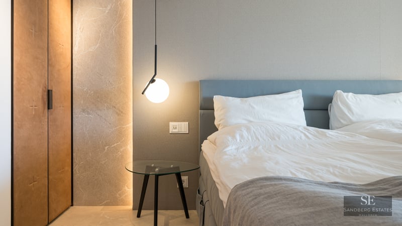 Luxury bedroom featuring a blue headboard, glass table, modern pendant light, and illuminated stone wall detail.