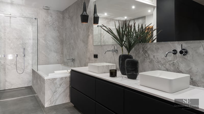Luxury bathroom with double white sinks, black vanity, marble-tiled bathtub, and a glass-enclosed walk-in shower.