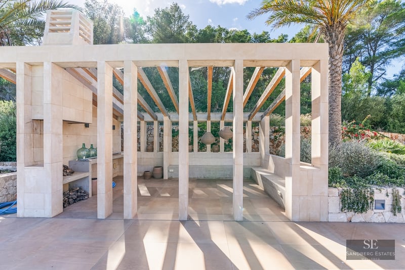 Modern stone pavilion with wooden rafters, outdoor fireplace, and built-in seating surrounded by lush greenery.