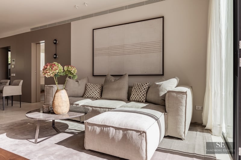 Minimalist living room featuring a large beige sectional sofa, marble coffee table, and large abstract wall art.