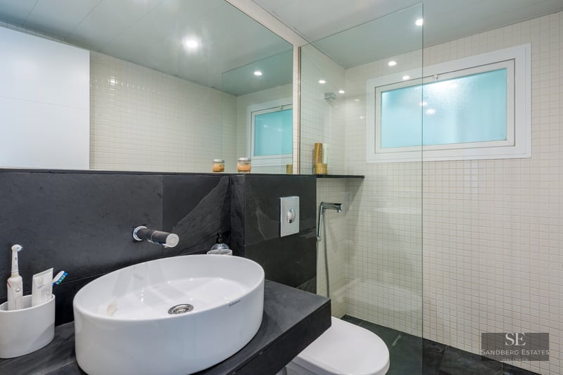 Modern bathroom featuring a white oval vessel sink on a dark slate counter, white mosaic tiles, and glass shower screen.