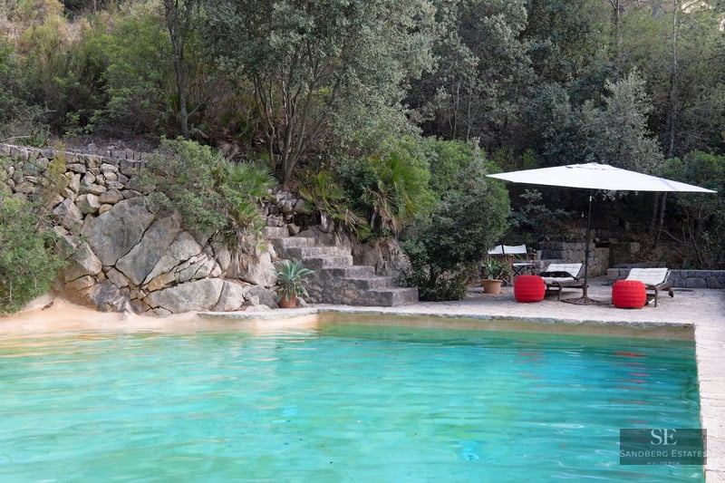 Turquoise swimming pool nestled against a natural rock wall with stone steps and lush greenery.