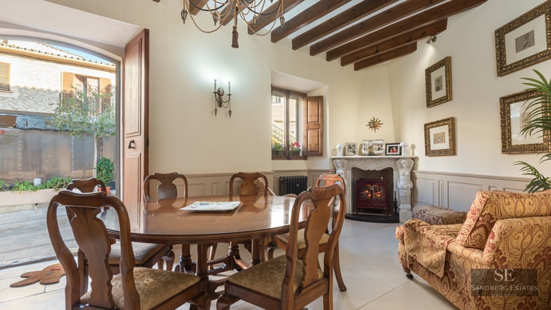 Elegant dining room with wooden table, exposed ceiling beams, and an ornate fireplace leading to an outdoor patio.