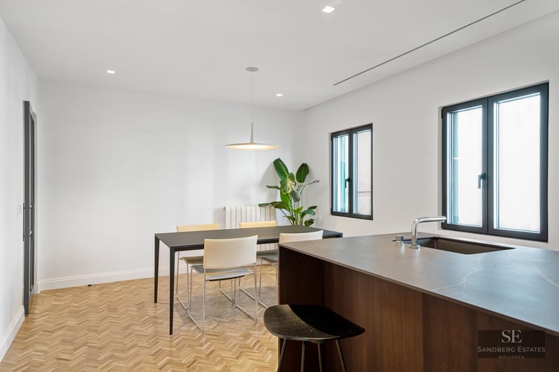 Modern dining room with black table, white chairs, herringbone wood floors, and a kitchen island.