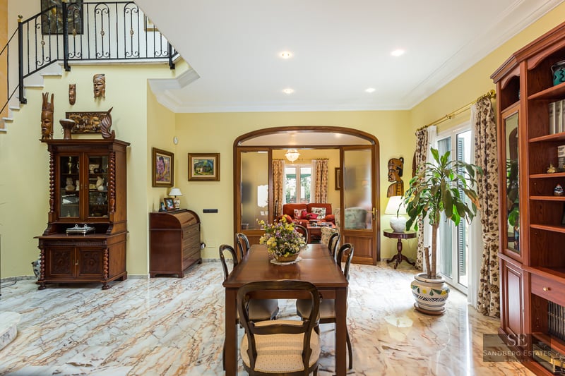 Spacious dining room featuring veined marble floors, classic wooden furniture, and African art decor.