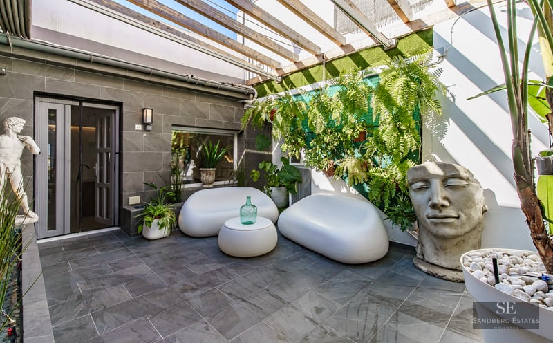 Contemporary patio with white curved sofas, stone tiles, wooden pergola, and a large stone face sculpture.