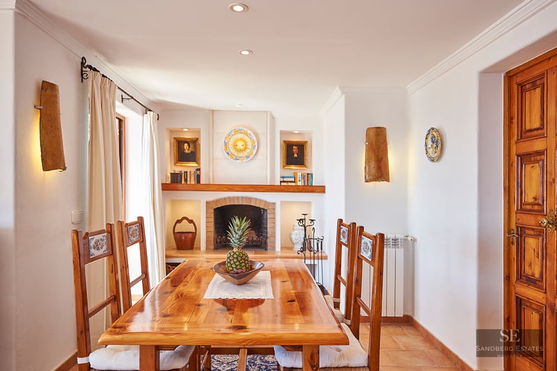 A wooden dining table and chairs in front of a brick fireplace in a Mediterranean-style room.