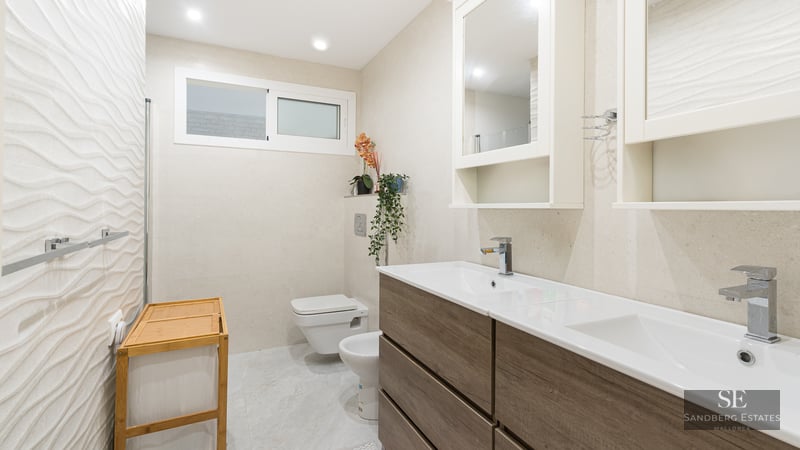 Modern bathroom with wood-finish double vanity, textured wall tiles, wall-hung toilet, and bidet.