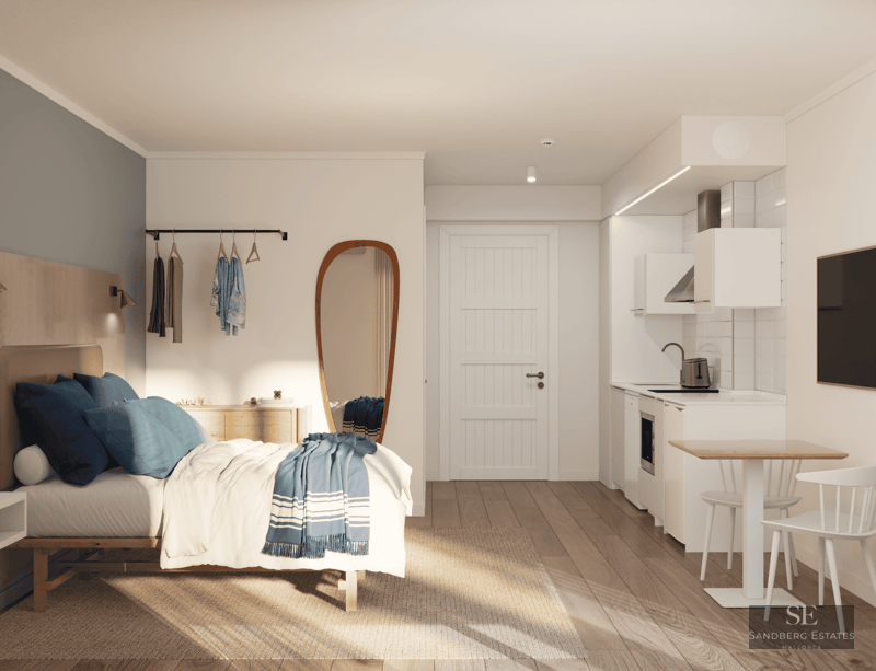 Studio lumineux avec lit aux accents bleus, cuisine blanche compacte et parquet en bois clair.