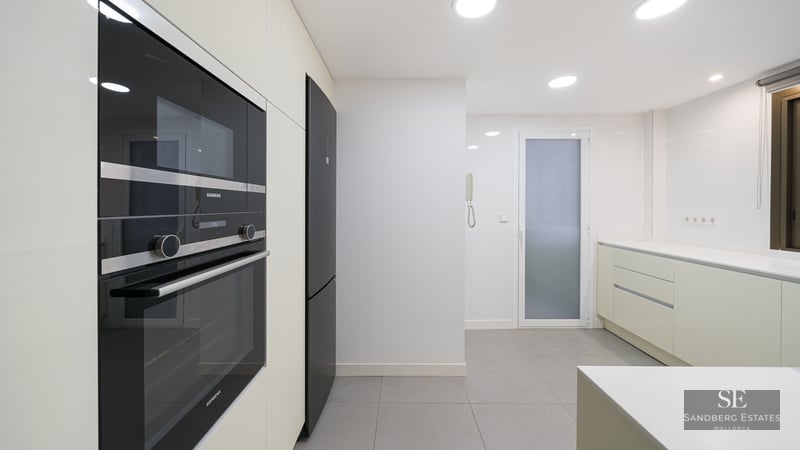 Modern white kitchen with built-in black Siemens oven and microwave, grey floor tiles, and recessed lighting.