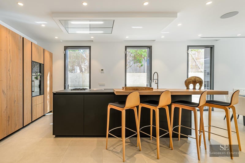 Modern kitchen featuring a black island with wooden breakfast bar, four stools, and floor-to-ceiling wooden cabinets.