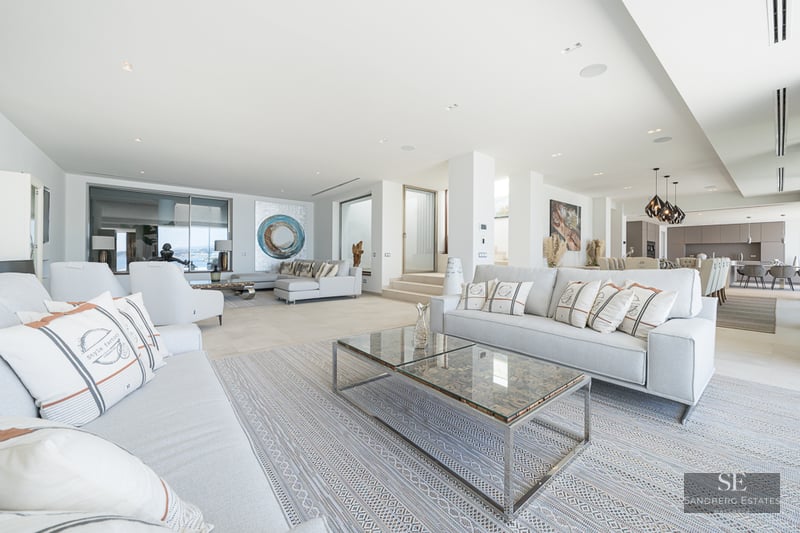 Spacious modern living room with grey sofas, glass coffee tables, and a view of the open-concept kitchen.