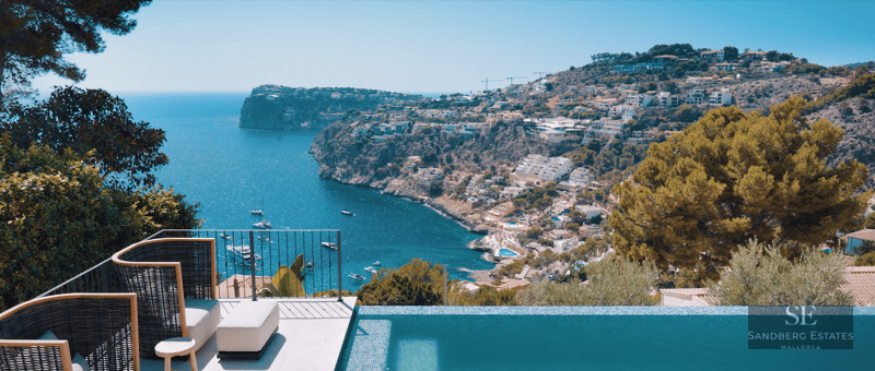 Luxury terrace featuring an infinity pool and designer lounge chairs overlooking a bay with yachts and cliffs.