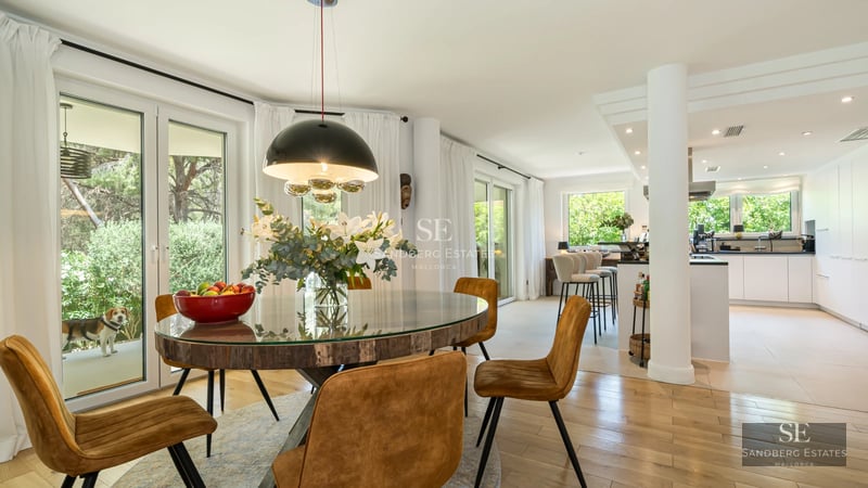 Spacious living room with windows overlooking the garden and pool. Modern design, light wood floors and minimalist furniture.