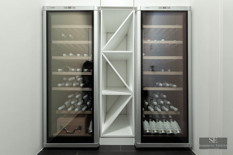 Two sleek silver Bosch wine fridges flanking a central white geometric bottle rack in a minimalist interior.