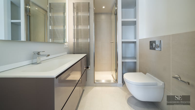 Modern bathroom with a large vanity, glass walk-in shower, wall-hung toilet, and chrome towel radiator.