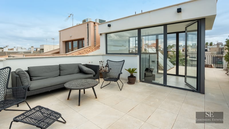 Rooftop terrace featuring grey sofa, black design chairs, and large glass doors with urban city views.