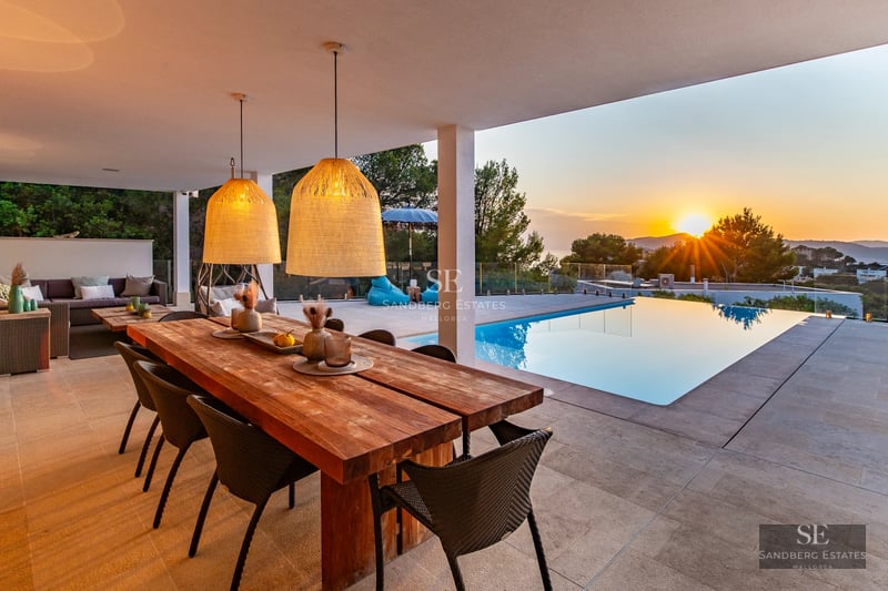 Exterior view of a modern villa with infinity pool, terrace, lush garden, and large windows providing natural light.