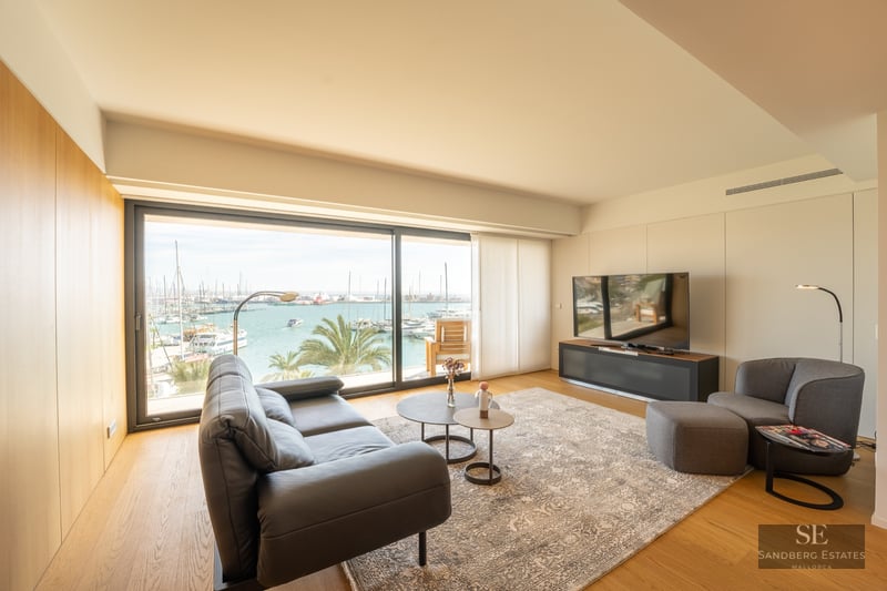 Modern living room with leather sofa and large glass windows overlooking a harbor with boats and palm trees.