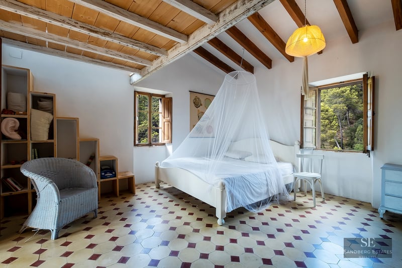 Bedroom featuring white walls, exposed wooden ceiling beams, patterned tile floor, and a bed with a mosquito net.