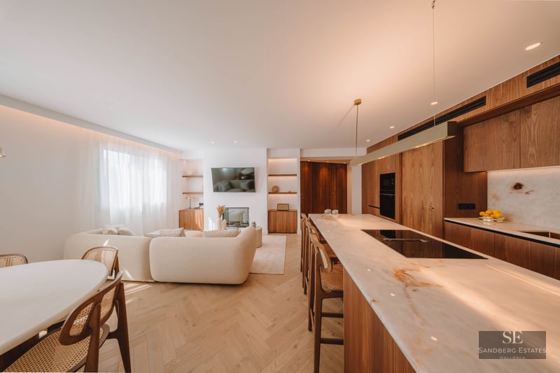 Bright open-concept living area with a beige sofa, marble kitchen island, and warm wood flooring.