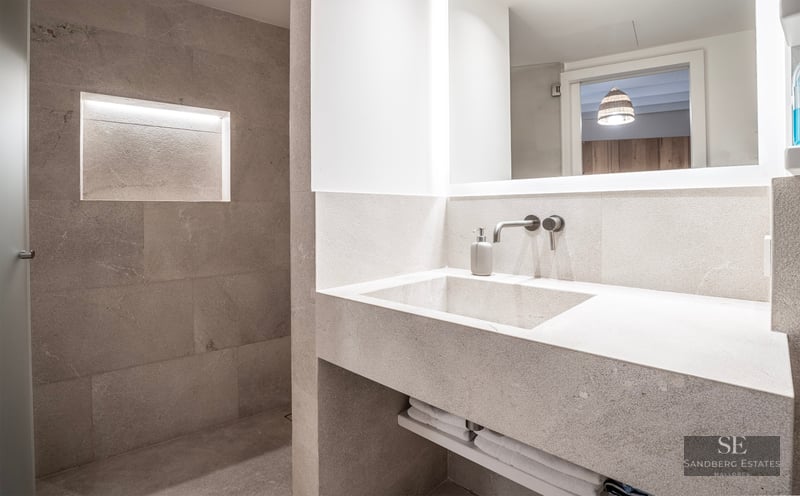 Modern bathroom featuring an integrated stone vanity, backlit mirror, and a walk-in shower with a lighted recessed niche.