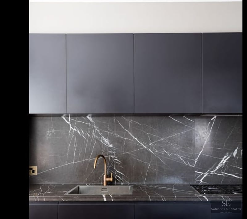 Close-up of a modern kitchen featuring a veined marble backsplash, brass faucet, and black cabinetry.