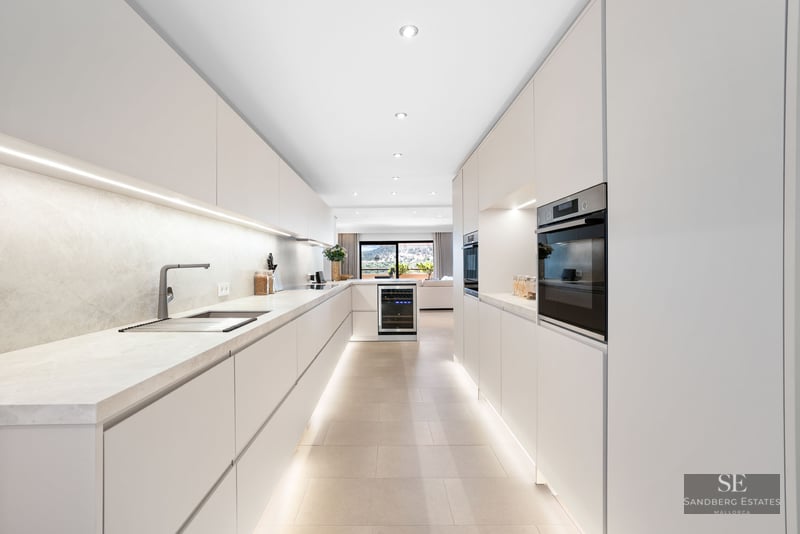 Cuisine moderne avec placards blancs sans poignées, plans de travail en marbre et éclairage LED intégré.