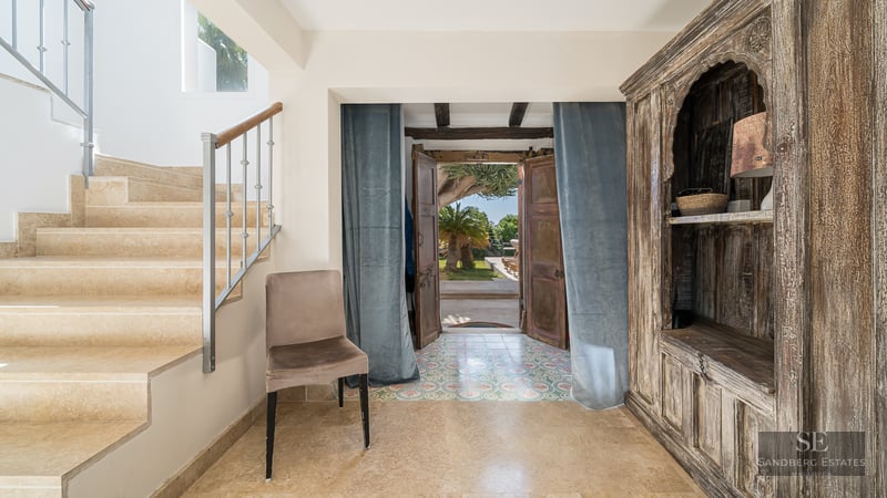 Entrance hall featuring a stone staircase, large antique wooden cabinet, and open doors leading to a sunny garden.