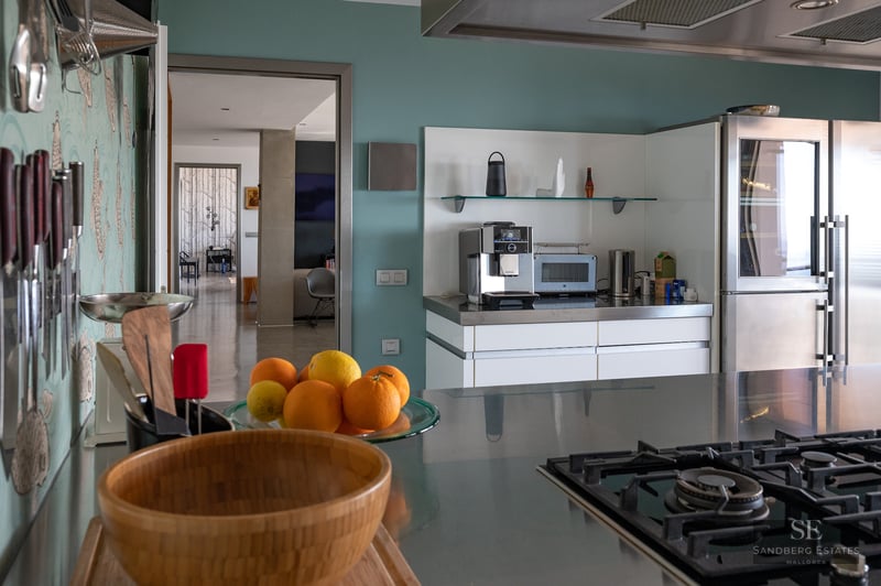 Modern kitchen featuring stainless steel countertops, a professional espresso machine, gas stovetop, and fresh citrus fruit.