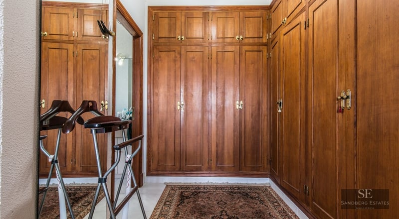 Walk-in closet with floor-to-ceiling wooden built-in wardrobes, Persian rug, and a valet stand.