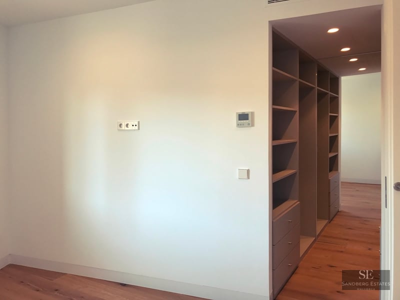 White room with light wood floors and a grey built-in shelving and drawer unit leading into a hallway.