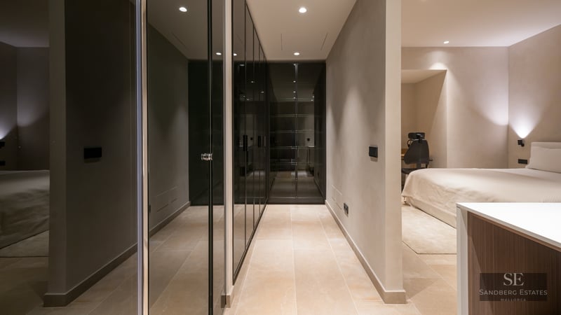 Minimalist master bedroom featuring sleek dark glass wardrobes, stone tile flooring, and warm recessed lighting.