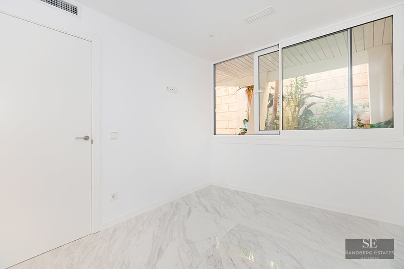 Empty room with white walls, polished marble floor, and a large sliding window overlooking outdoor greenery.