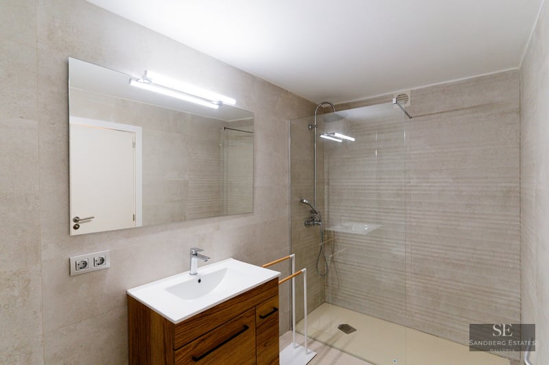 Contemporary bathroom featuring a walk-in glass shower, stone tiles, and a wooden vanity with a large mirror.