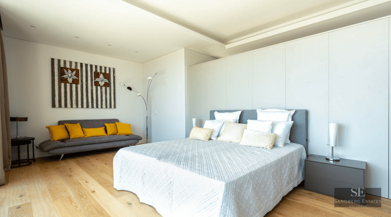 Bright modern bedroom featuring a large bed, wooden floors, and a grey sofa with yellow pillows.