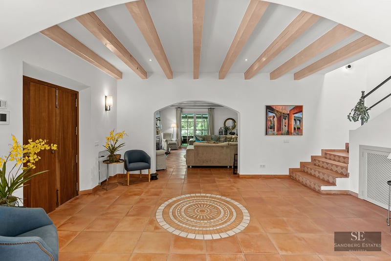 Entryway with wooden ceiling beams, terracotta floors, an arched doorway to the living room, and a tiled staircase.