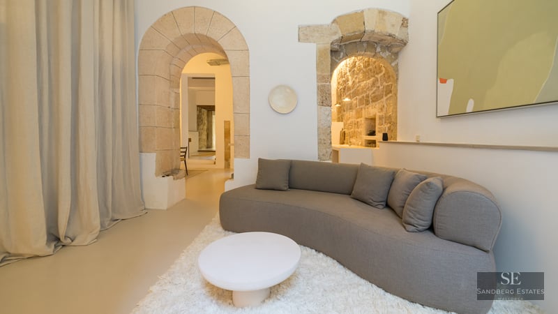 Modern curved gray sofa and white shag rug next to ancient stone archways in a minimalist living room.