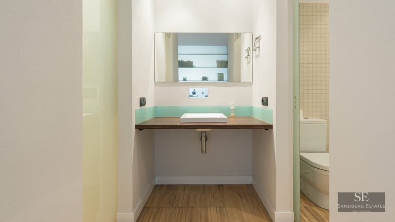 Bathroom featuring a floating wood countertop, white square vessel sink, rectangular mirror, and teal glass backsplash.