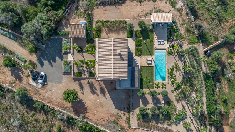 Bird's eye view of a modern villa with a turquoise pool, landscaped gardens, and terracotta roofs.