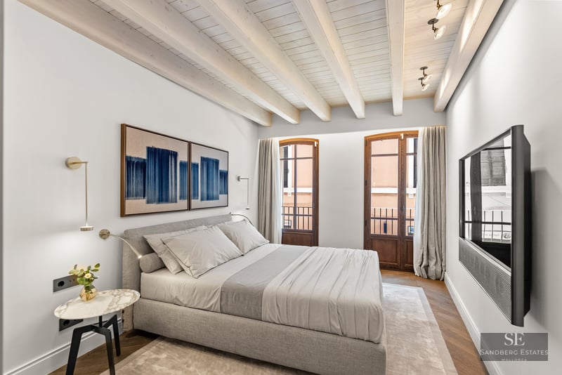 Modern bedroom featuring a grey bed, white wooden beams, French doors, and blue abstract wall art.
