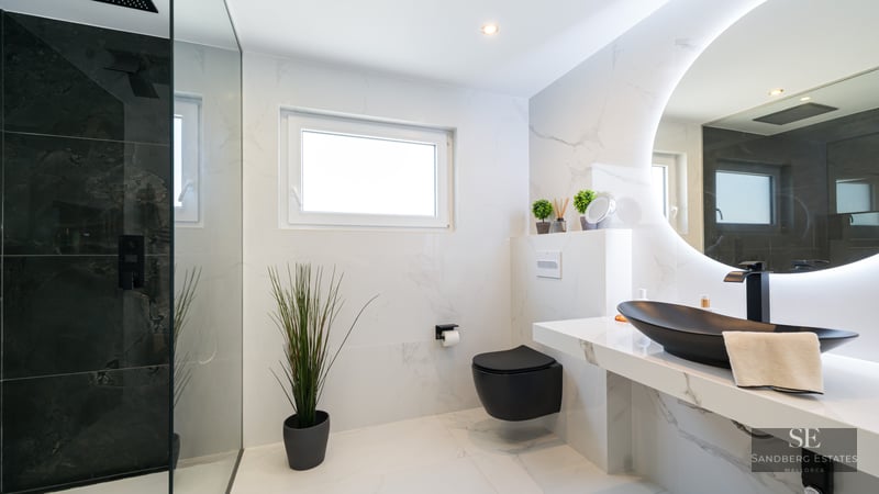 Salle de bain élégante avec carrelage en marbre blanc, lavabo noir, miroir rétroéclairé et douche à l'italienne.