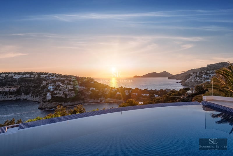 Modern terrace with infinity pool, sea views, designer furniture, and wooden flooring. Glass railing and lush vegetation.