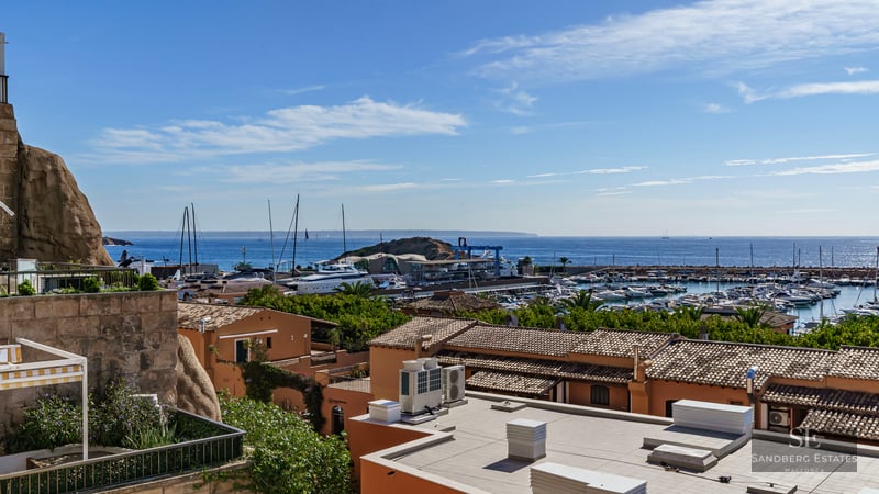 Elevated view of a Mediterranean marina with terracotta roofs, white yachts, and the blue sea under a clear sky.
