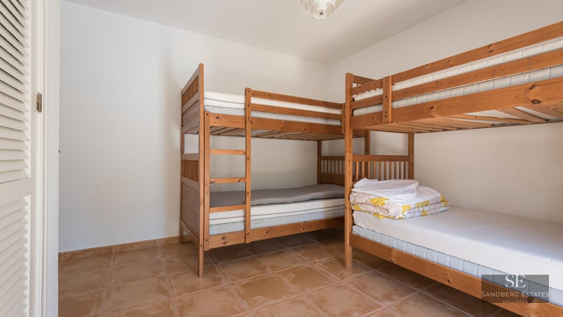 A bright bedroom with two wooden bunk beds and terracotta tiled floors.