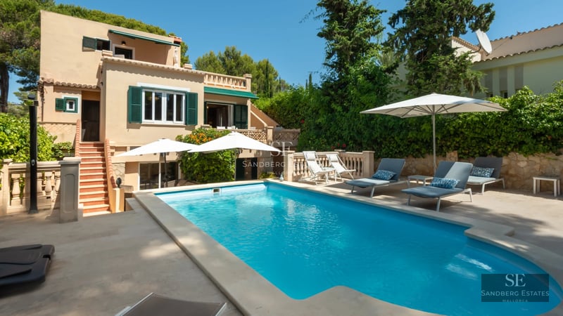Expansive pool surrounded by lush garden, sun loungers, and a modern house with large windows inviting relaxation.