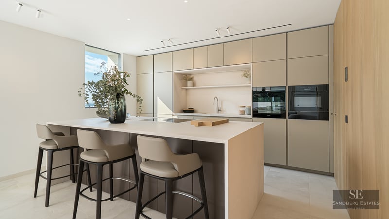 Modern minimalist kitchen featuring a large central island, designer bar stools, and sleek earth-toned cabinetry.