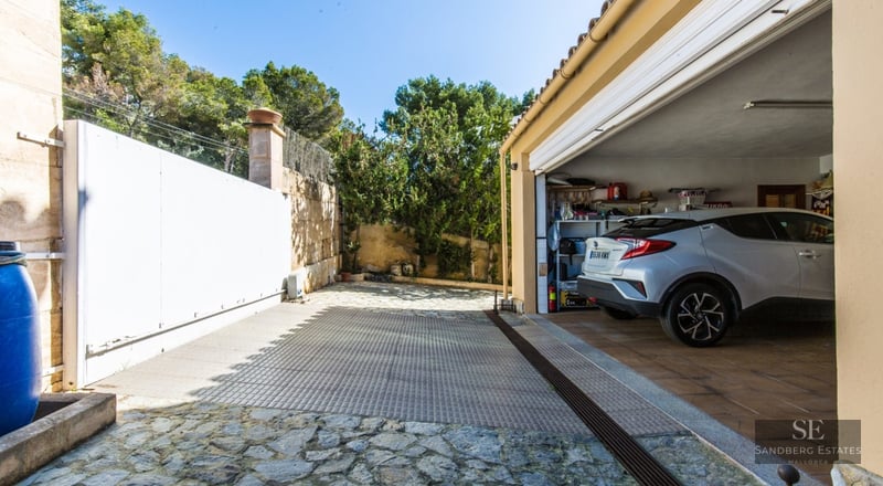 Car parked in a spacious garage next to a natural stone driveway with a large white sliding gate.